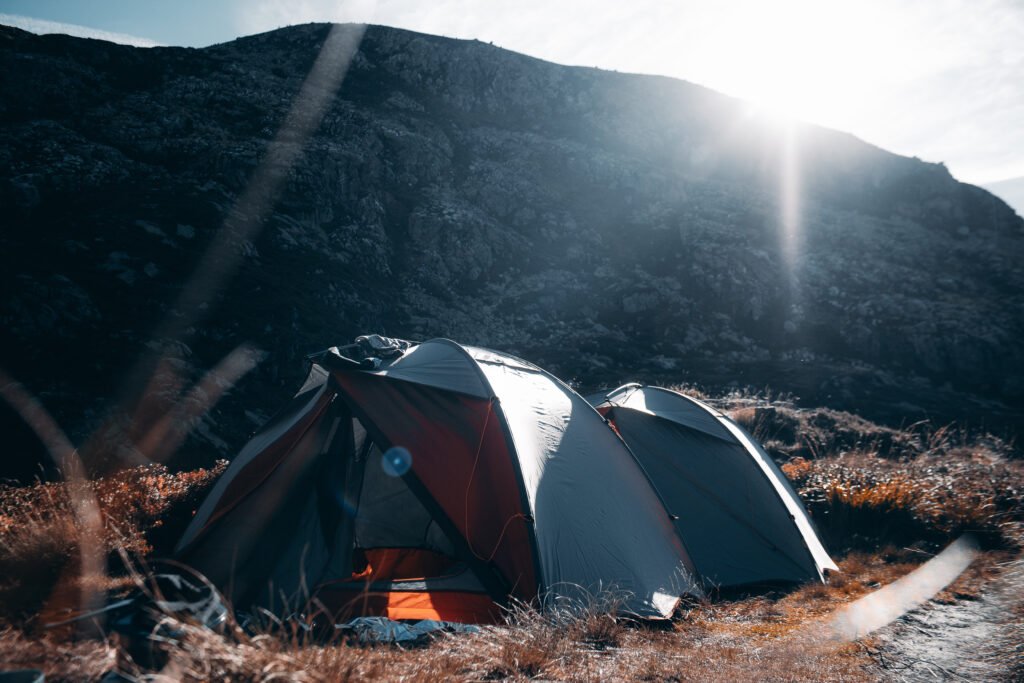 Deux tentes de bivouac installées en pleine montagne au bord d’un lac, dans un paysage naturel isolé et paisible.